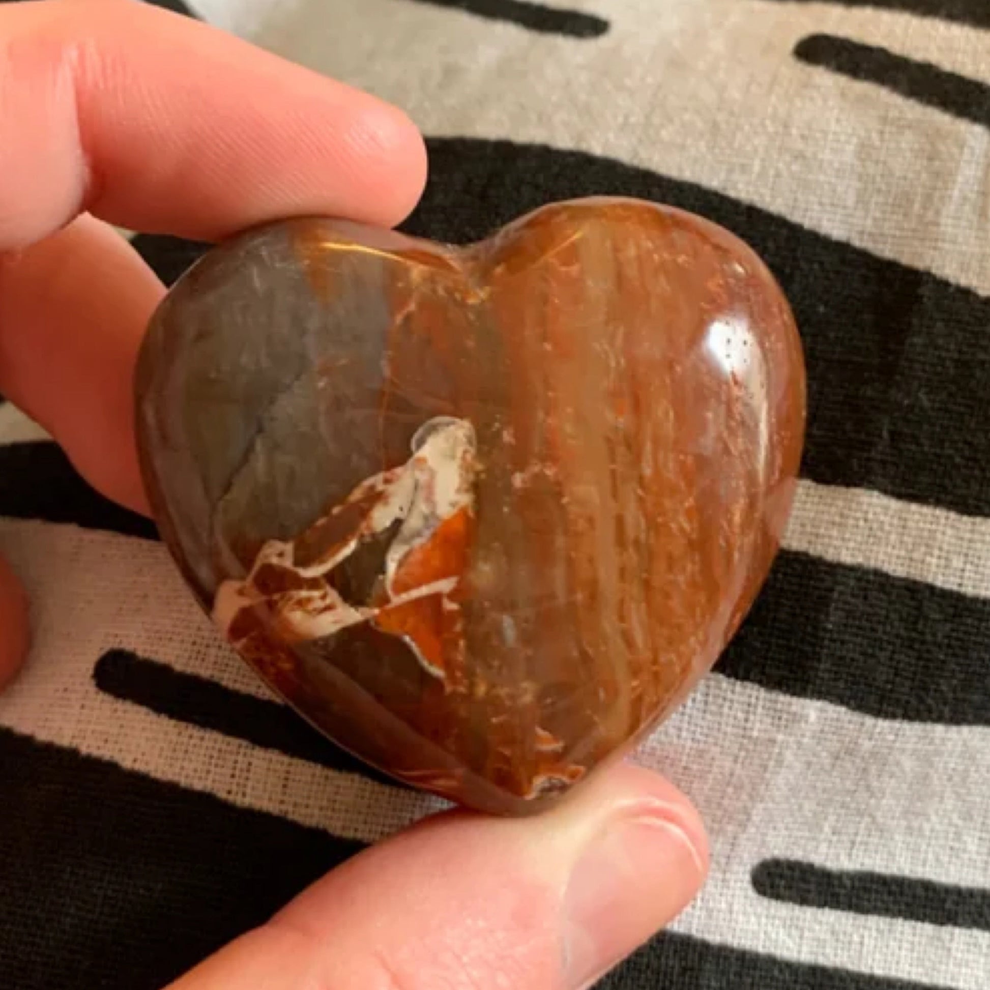 Hand holding a polished red petrified wood heart with natural patterns on fabric background