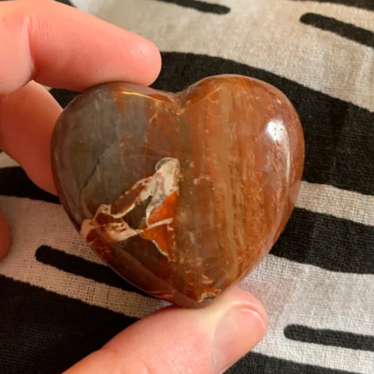 Hand holding a polished red petrified wood heart with natural patterns on fabric background