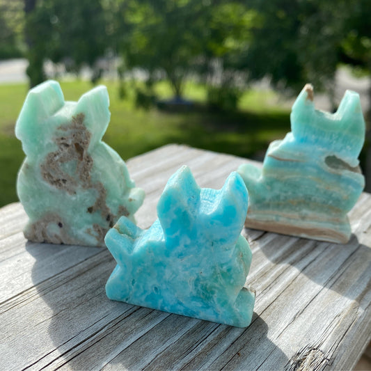 Three carved hemimorphite cats in blue and green shades placed on wooden surface outdoors
