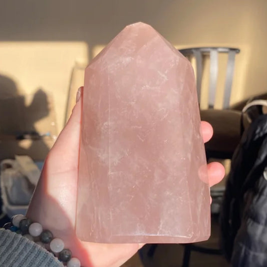 Hand holding a polished lavender rose quartz tower crystal in soft natural light