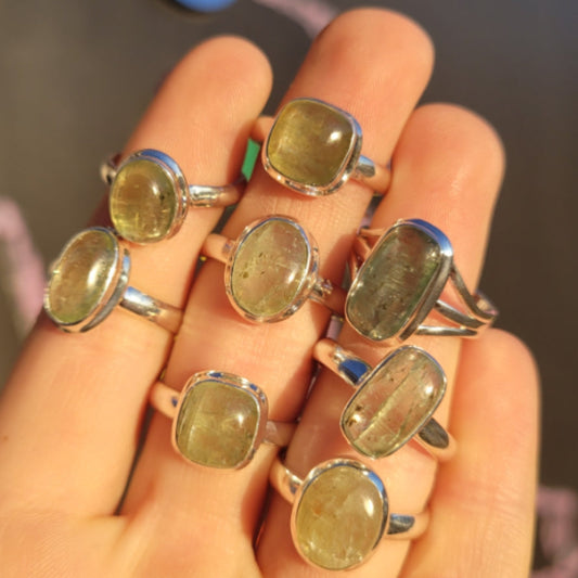Hand displaying multiple silver rings with natural mint green kyanite gemstones in various shapes and sizes