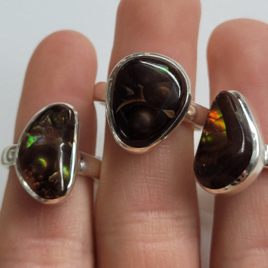 Close-up of three silver rings featuring dark fire agate stones with iridescent flashes worn on fingers