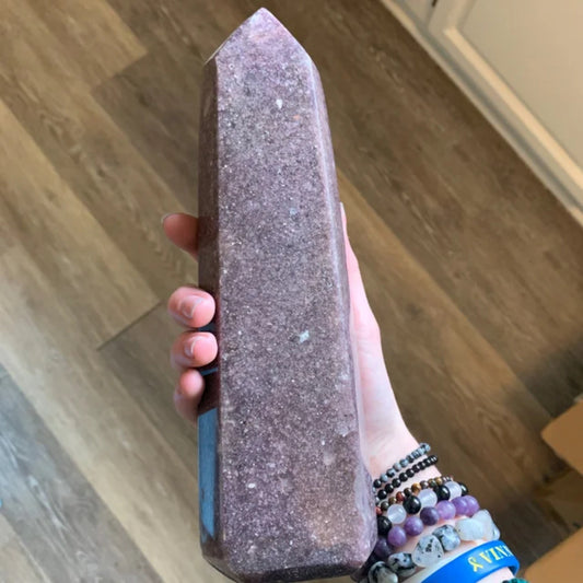 Large lepidolite tower crystal held in hand on wooden floor background