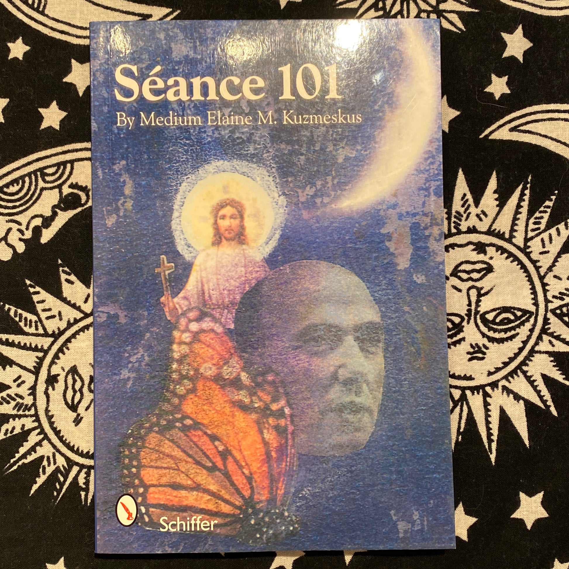 Book cover of Séance 101 by Medium Elaine M. Kuzmeskus featuring a mystical blue background with a monarch butterfly, a human face, and a glowing figure holding a cross under a crescent moon