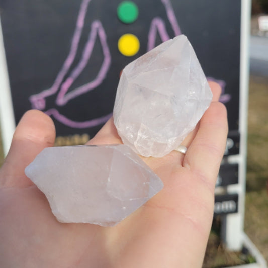 Hand holding two clear quartz points with a chakra board in the background