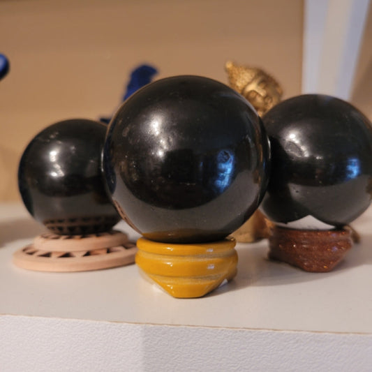 Black Tourmaline Sphere on a yellow stand with other black spheres and decorative items in the background