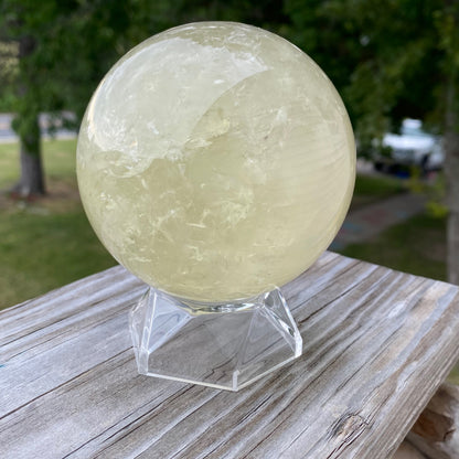 Polished citrine sphere crystal on clear stand with outdoor background