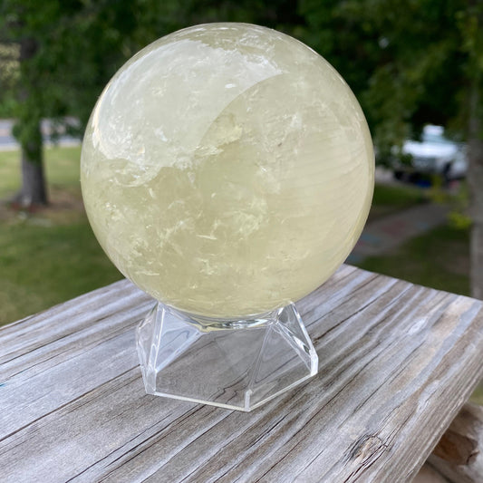 Polished citrine sphere crystal on clear stand with outdoor background