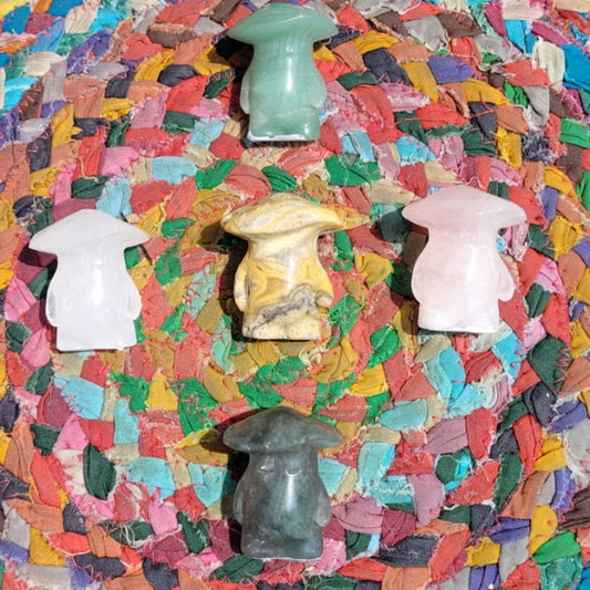 Five colorful crystal mushroom man figurines arranged on a multicolored woven mat