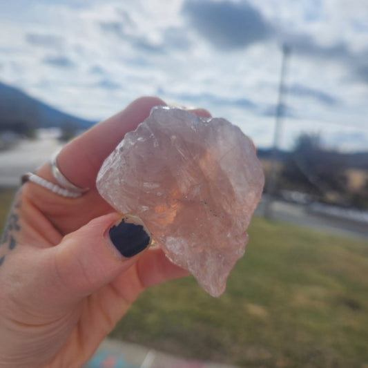 Raw rose quartz palm sized crystal held in hand with natural unpolished texture and soft pink hue