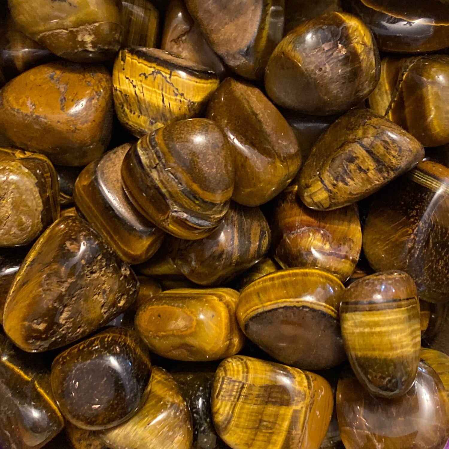 Close-up of polished Tigers Eye tumble stones with golden brown banding and smooth surfaces.