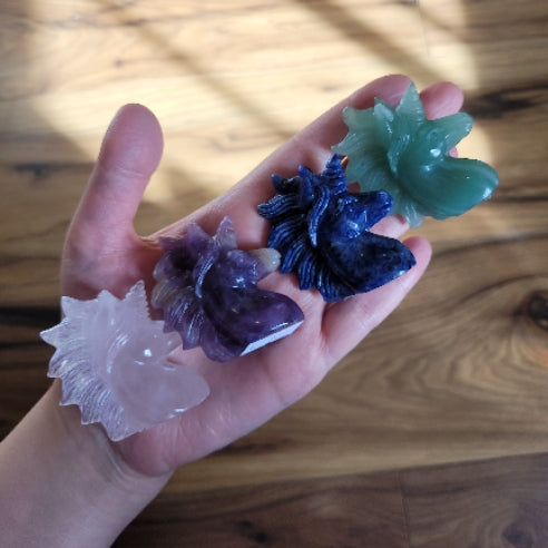 Hand holding four colorful crystal unicorn figurines in pink, purple, blue, and green on wooden background