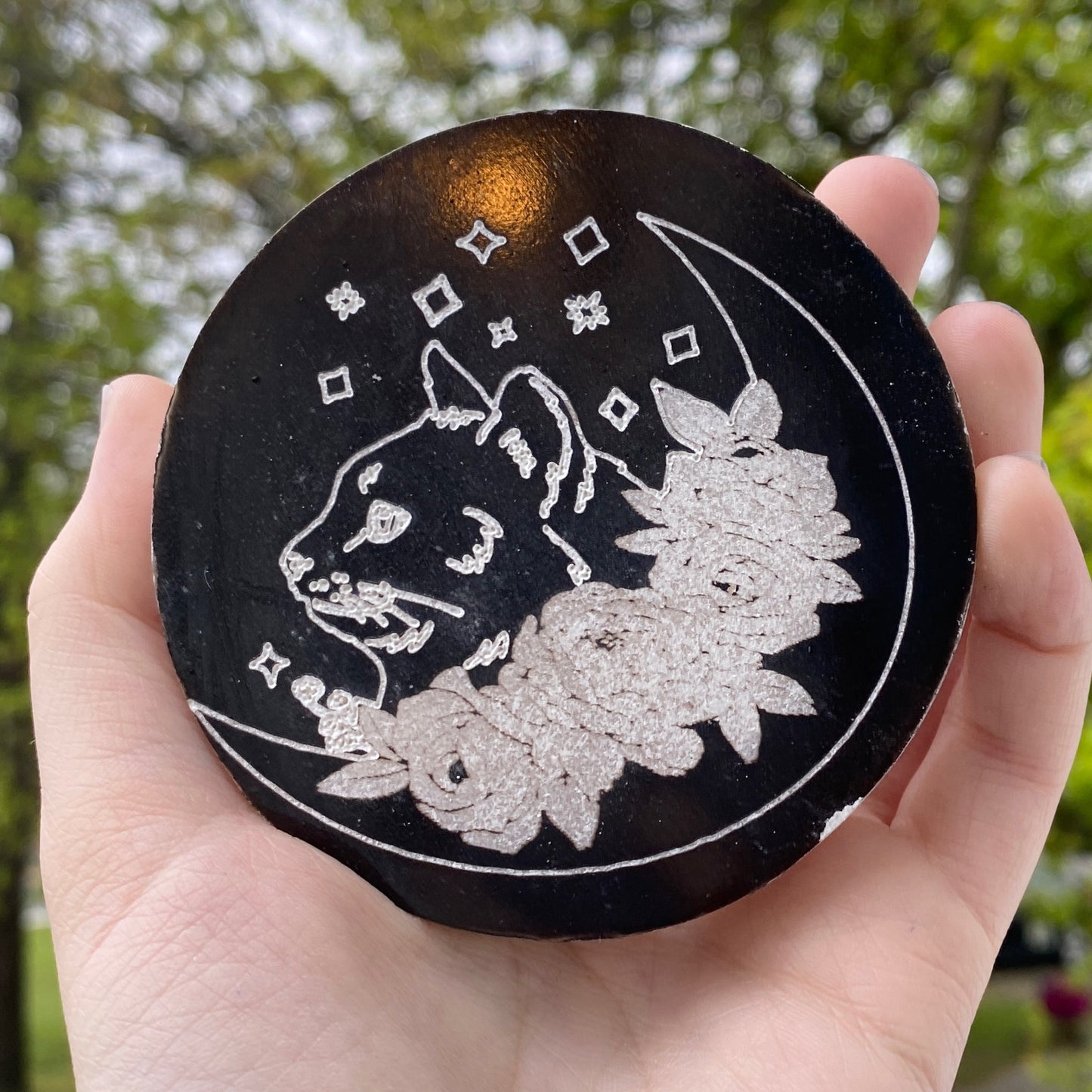 Selenite black cat plate with engraved floral and celestial design held in hand outdoors