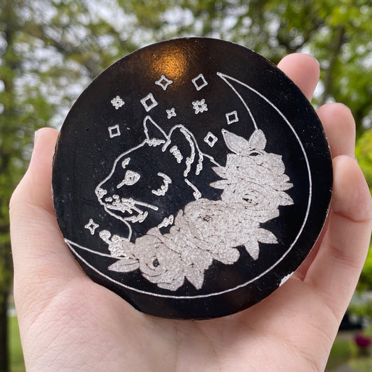 Selenite black cat plate with engraved floral and celestial design held in hand outdoors