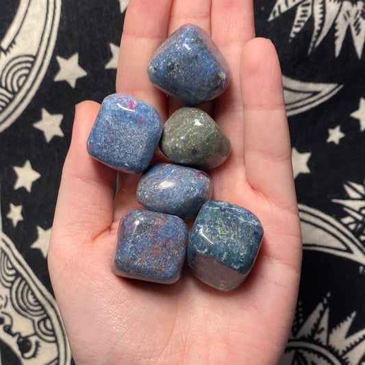Hand holding polished Kyanite stones with Ruby tumbles on a patterned black and white background