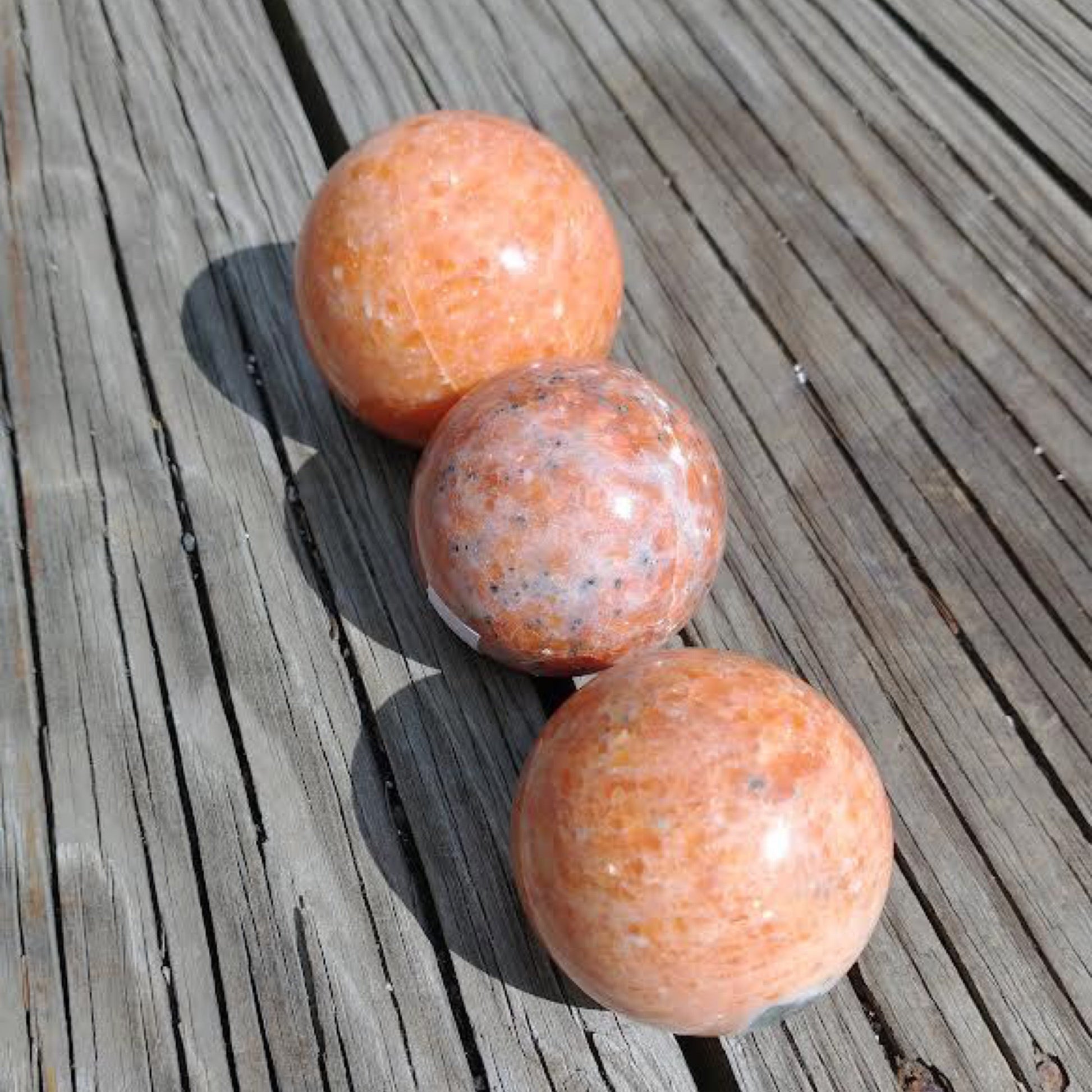 Three polished sunstone spheres on wooden surface