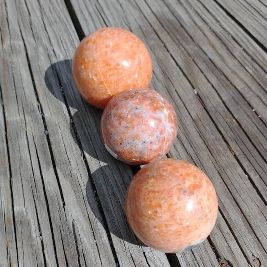 Three polished sunstone spheres on wooden surface