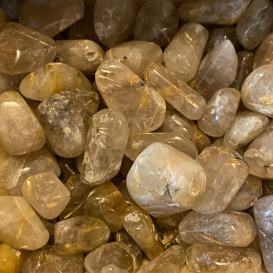 Close-up of polished rutilated quartz tumble stones with golden needle-like inclusions