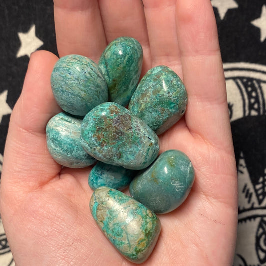 Hand holding polished blue-green Chrysocolla tumble stones on star-patterned background