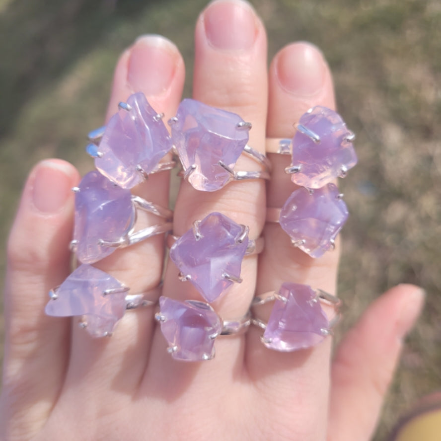 Hand displaying multiple rings featuring raw lavender quartz stones in silver settings, showcasing natural variations in shape and color.