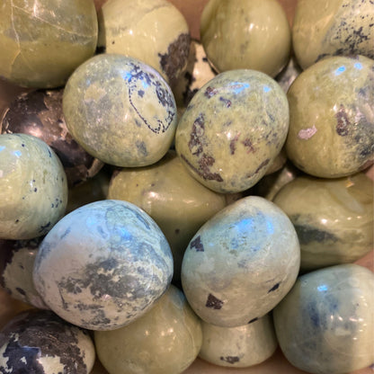 Close-up of polished serpentine tumble gemstones with natural greenish hues and dark inclusions for energy and flexibility benefits
