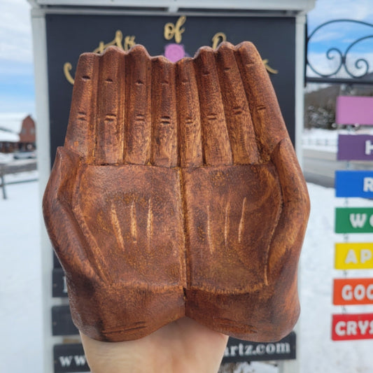 Wooden hand carving bowl shaped like two cupped hands with detailed finger and palm designs held outdoors