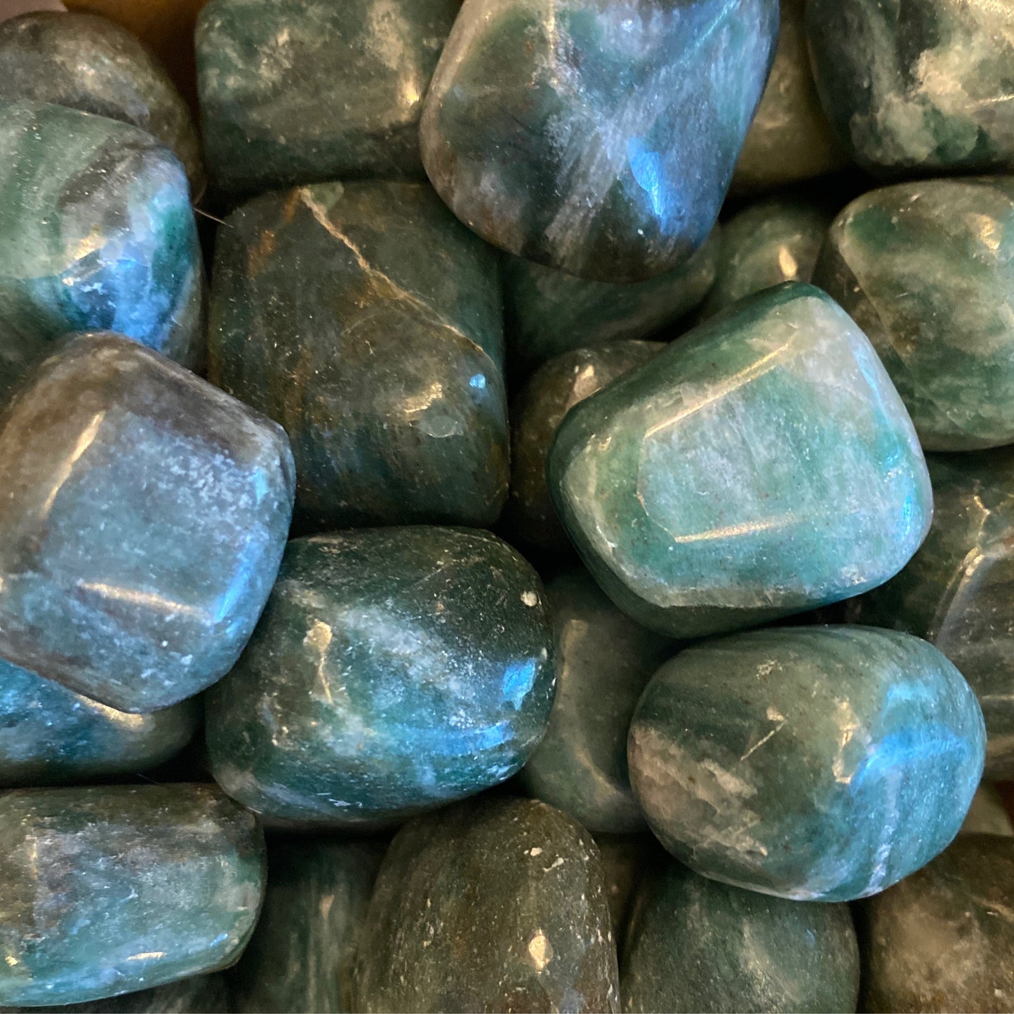 Close-up of polished tumble emerald gemstones with fuschite inclusions showing deep green and blue tones