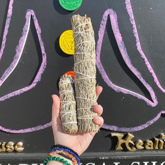 Hand holding two bundles of Blue Sage sticks with colorful chakra symbols and chalk drawings in background