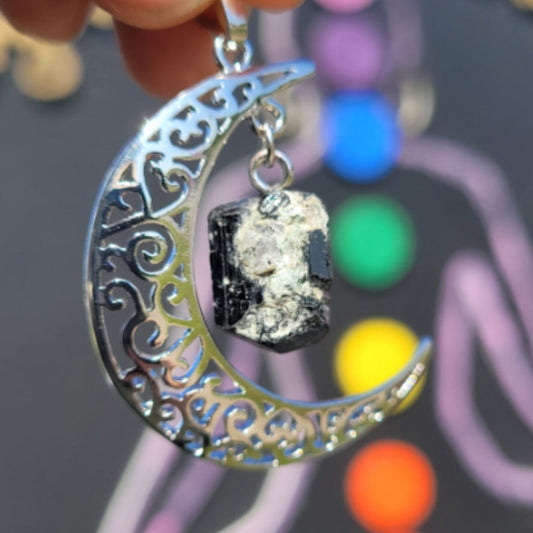 Silver crescent moon pendant with intricate cut-out designs and a hanging crystal stone centerpiece