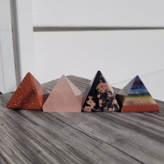 Set of colorful crystal pyramids including a Rhodonite pyramid on wooden surface