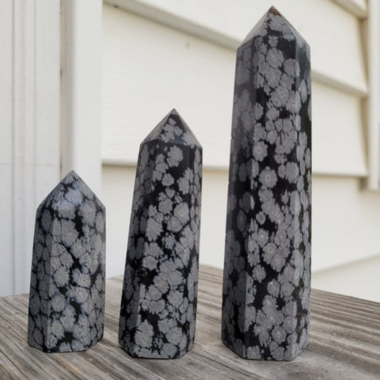 Set of three polished Snowflake Obsidian Towers with gray and black snowflake patterns on wooden surface