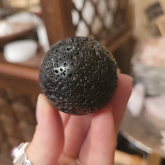 Black textured lava sphere held in hand with perforated surface details