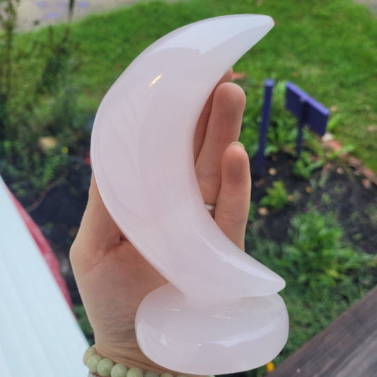 pink calcite moon sculpture on stand held in hand with garden background