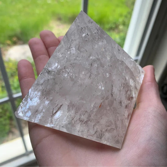 Clear quartz pyramid held in hand with natural background outdoors