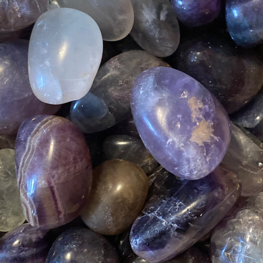 Close-up of polished rainbow fluorite tumble stones in various purple, blue, and white shades