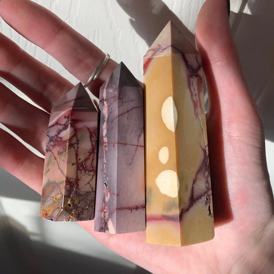 Hand holding three polished Mookaite Towers in different colors and patterns with natural sunlight.