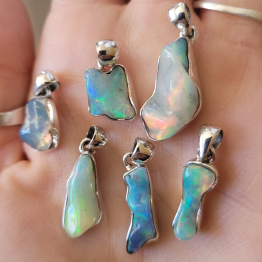 Collection of natural Ethiopian opal pendants with silver settings displayed on a hand