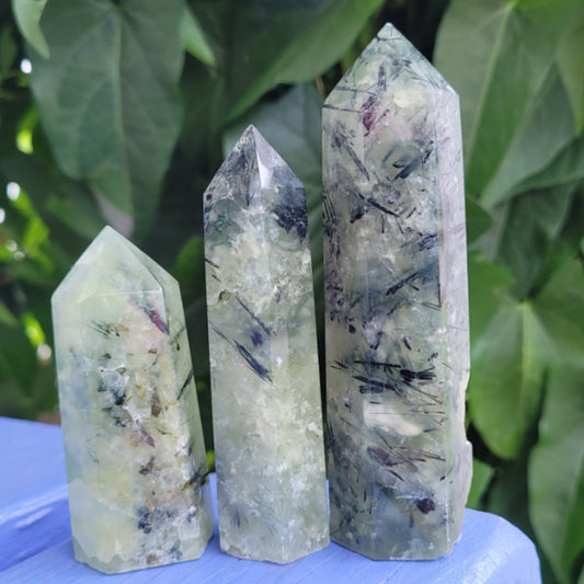 Three natural Prehnite towers with varying sizes and patterns on a blue surface against green leaves background