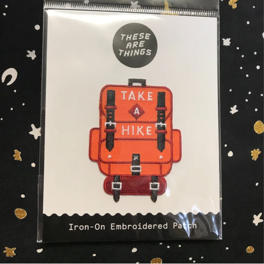 Take A Hike iron-on embroidered patch featuring an orange backpack design with hiking straps and text "TAKE A HIKE"
