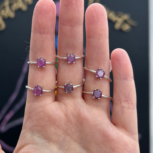 Hand displaying six silver rings each set with a unique natural ruby stalactite gemstone in deep red hues against a dark background