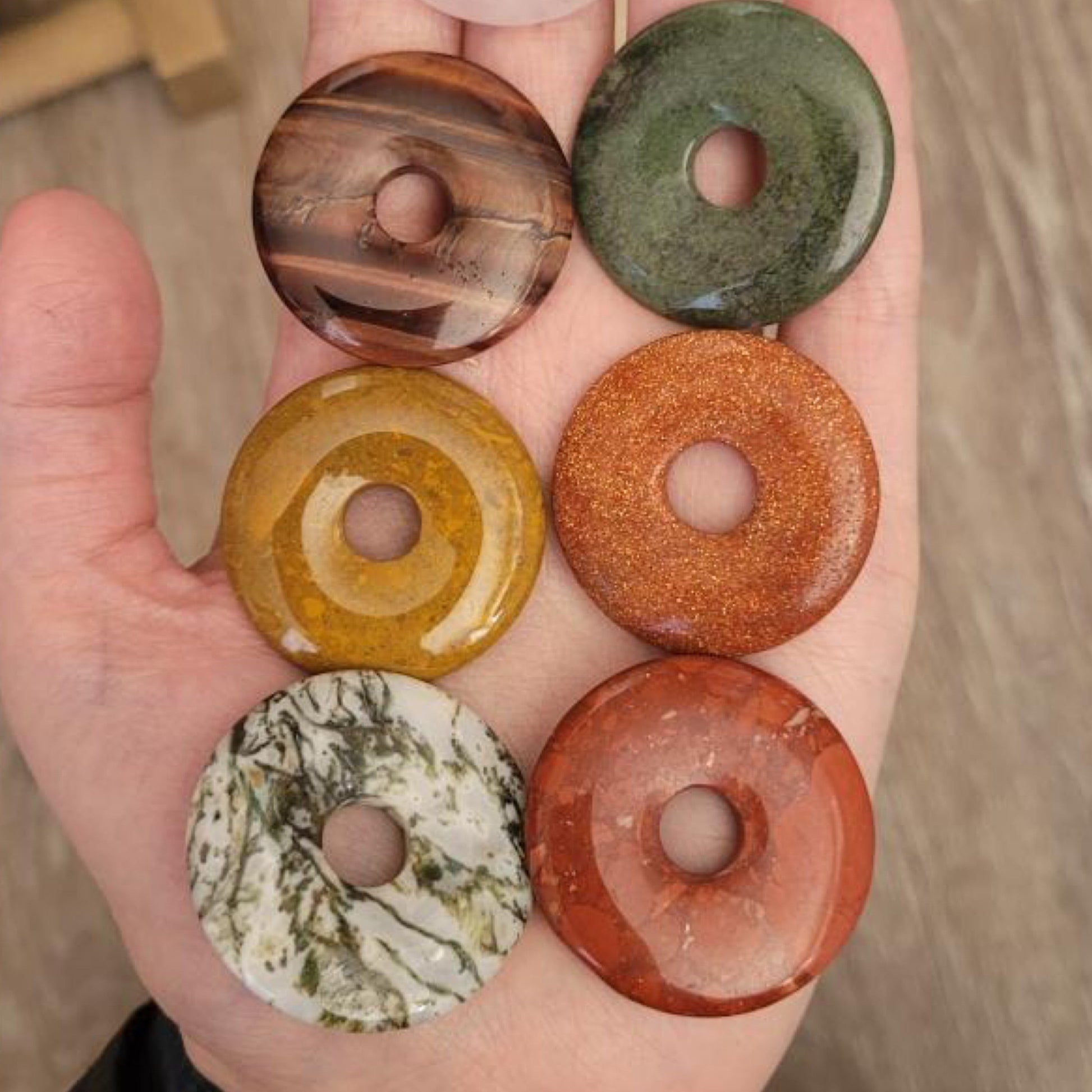 Hand holding six assorted crystal pi donut stones in various colors promoting energy flow and creativity
