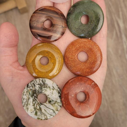 Hand holding six assorted crystal pi donut stones in various colors promoting energy flow and creativity