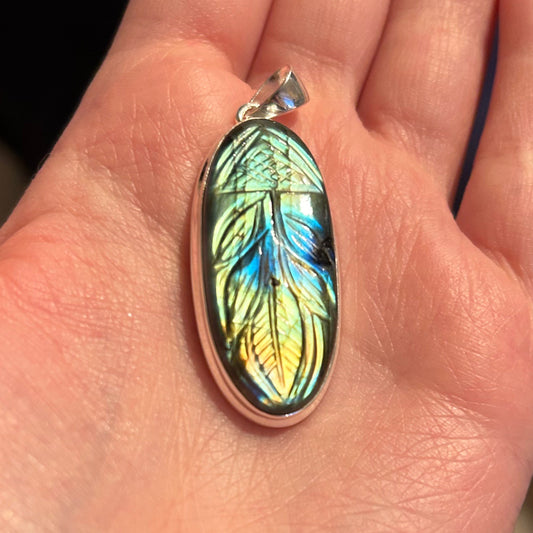 Labradorite hand carved pendant with iridescent feather design held in hand