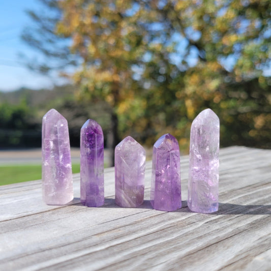Set of five 1-2 inch amethyst obelisk towers on wooden surface with blurred outdoor background