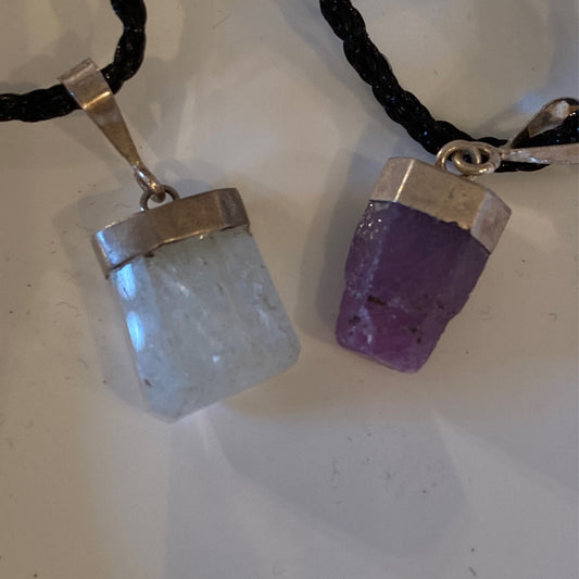 Two polished crystal pendants on black cords with silver caps, one clear and one purple