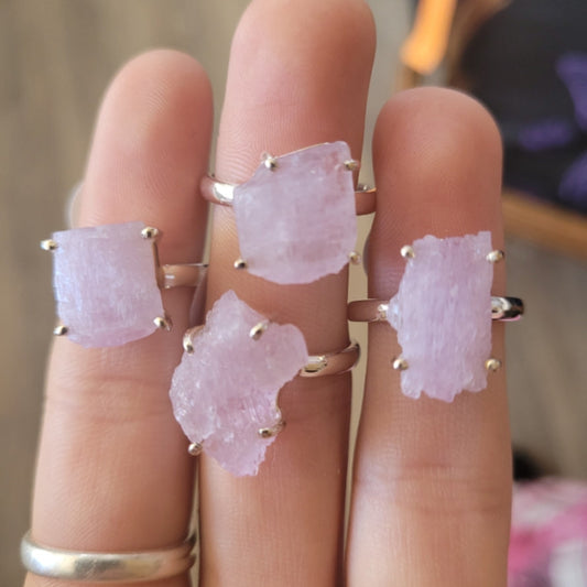 close-up of four raw kunzite rings on fingers with silver bands and light pink gemstones