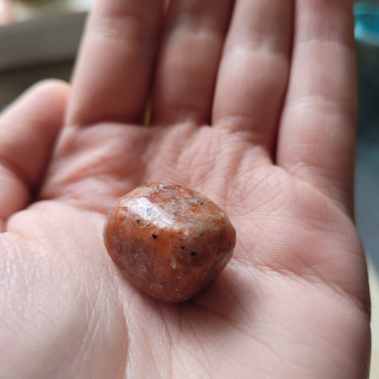 Tumbled orchid calcite stone held in hand showcasing smooth orange and pink hues