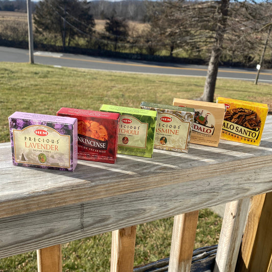 HEM Assorted Incense Cones collection including lavender, frankincense, patchouli, jasmine, sandalwood, and palo santo flavors displayed outdoors on wooden railing.