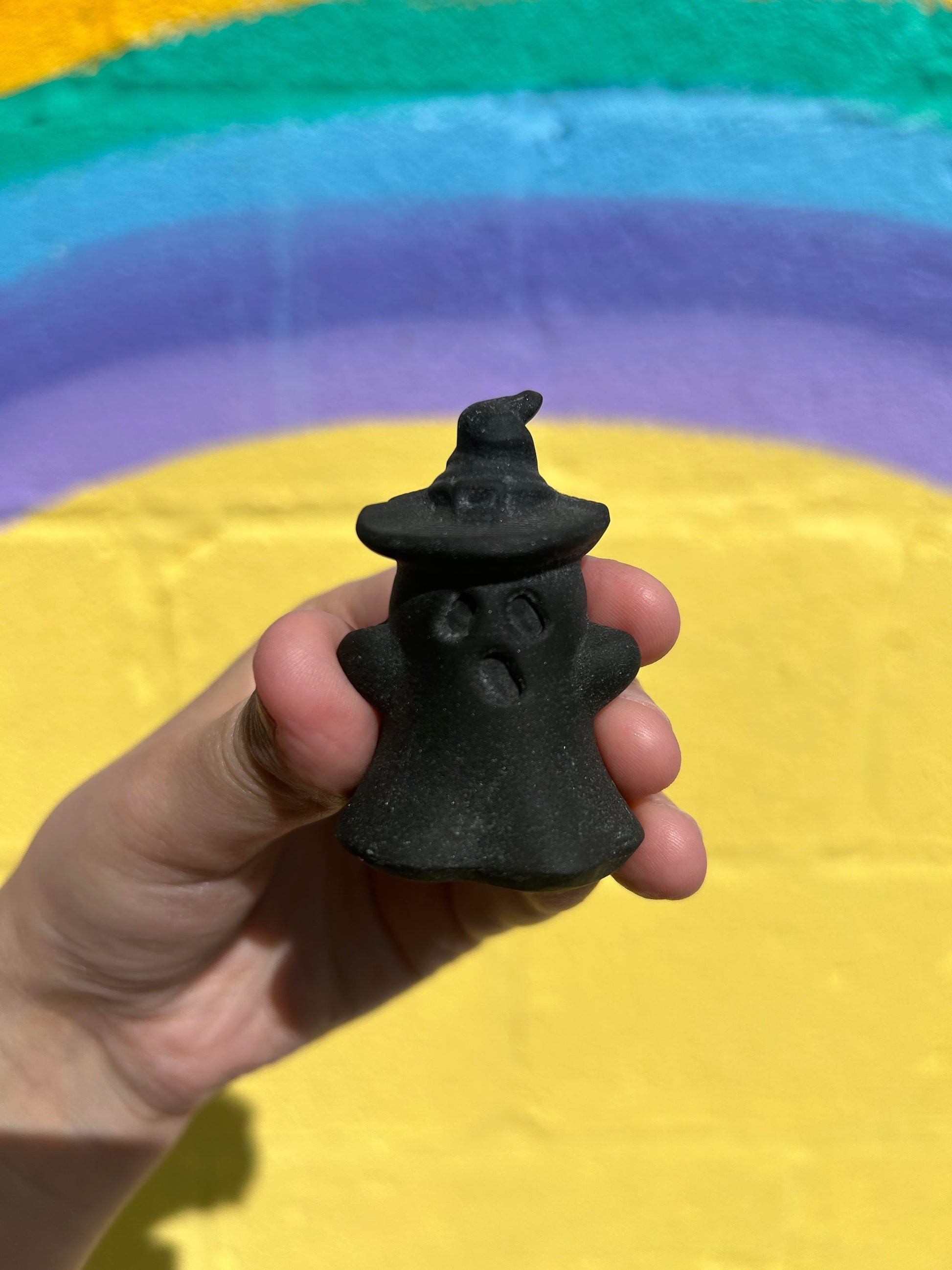 Hand holding black obsidian wizard ghost carving with colorful rainbow background