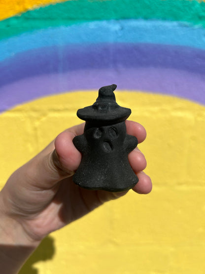 Hand holding black obsidian wizard ghost carving with colorful rainbow background